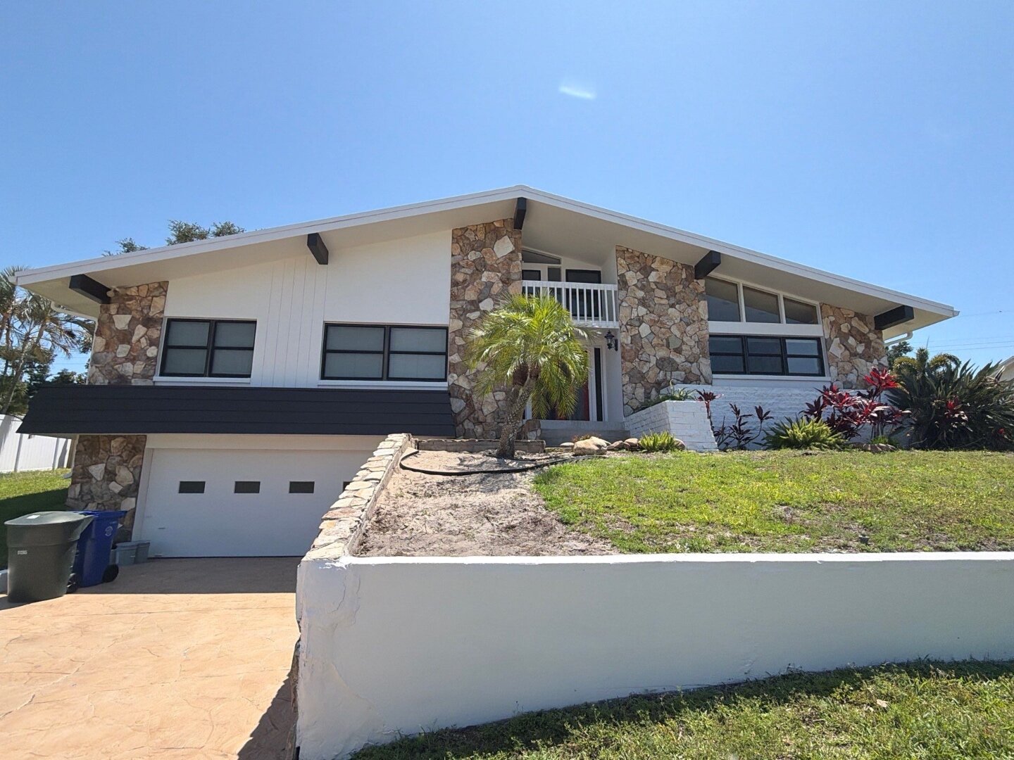 Dunedin Florida mid-century home exterior after painting by Highmark Painters and Handymen, in fresh white Sherwin-Williams Duration with dark trim accents and stone facade highlighted