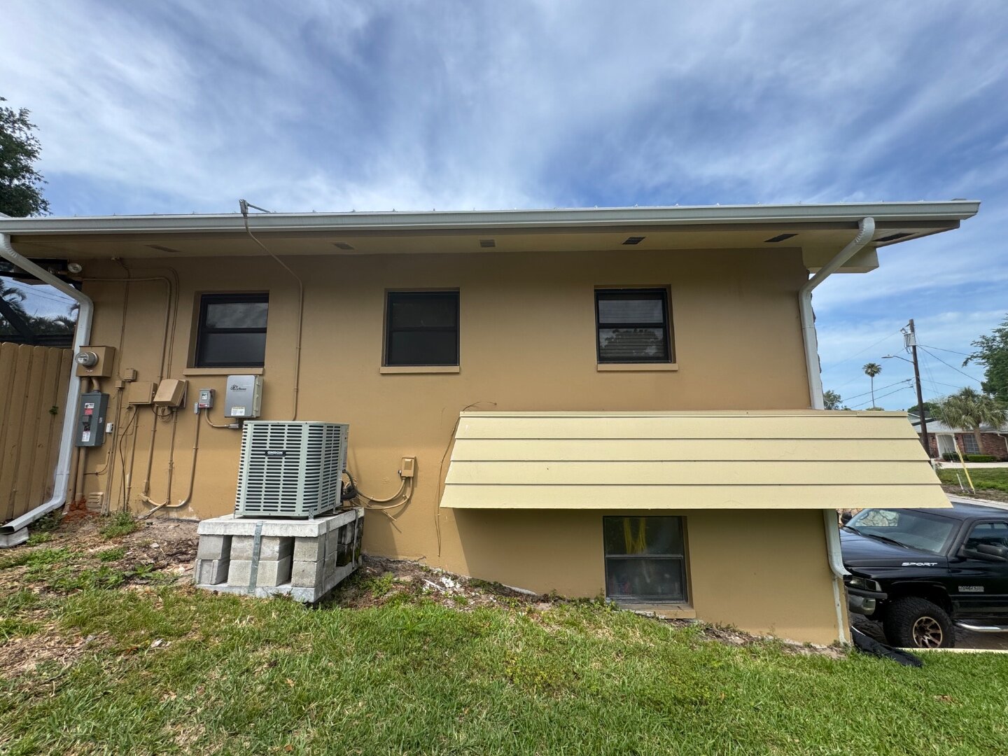Dunedin home side wall before painting with original tan stucco and yellow AC cover